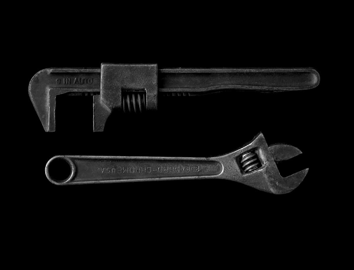 Two well-worn pipe wrenches photographed on a dark background