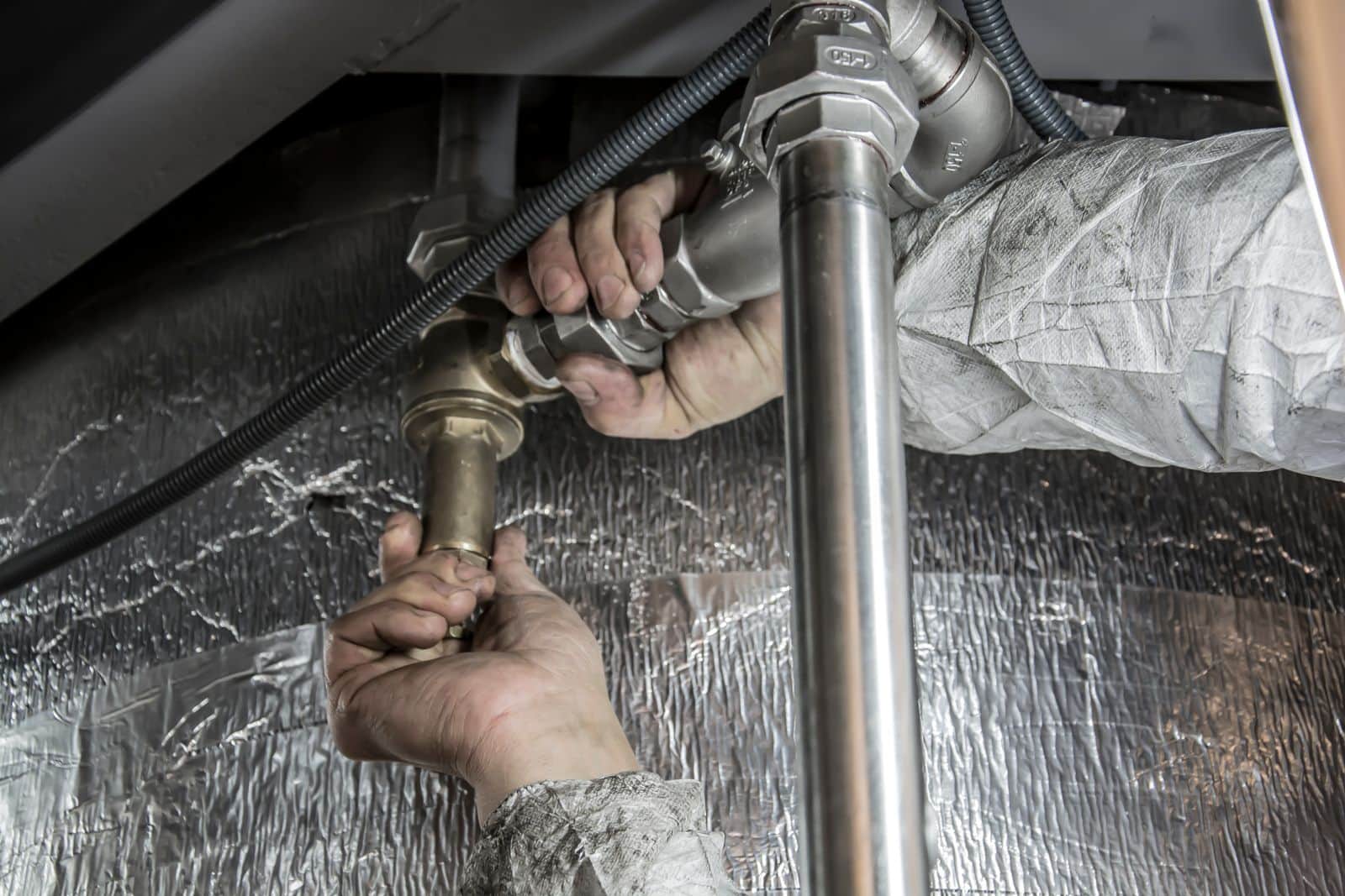 A plumber's hands tightening a brass union fitting on a supply line