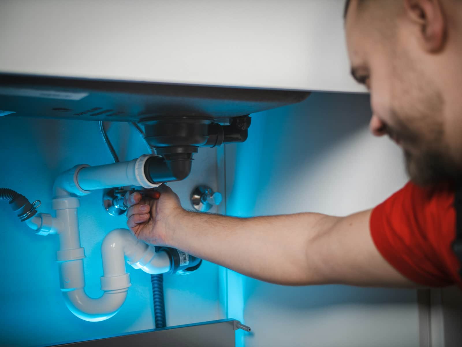 Plumber reaching into an under-sink cabinet to repair a leaking drain trap