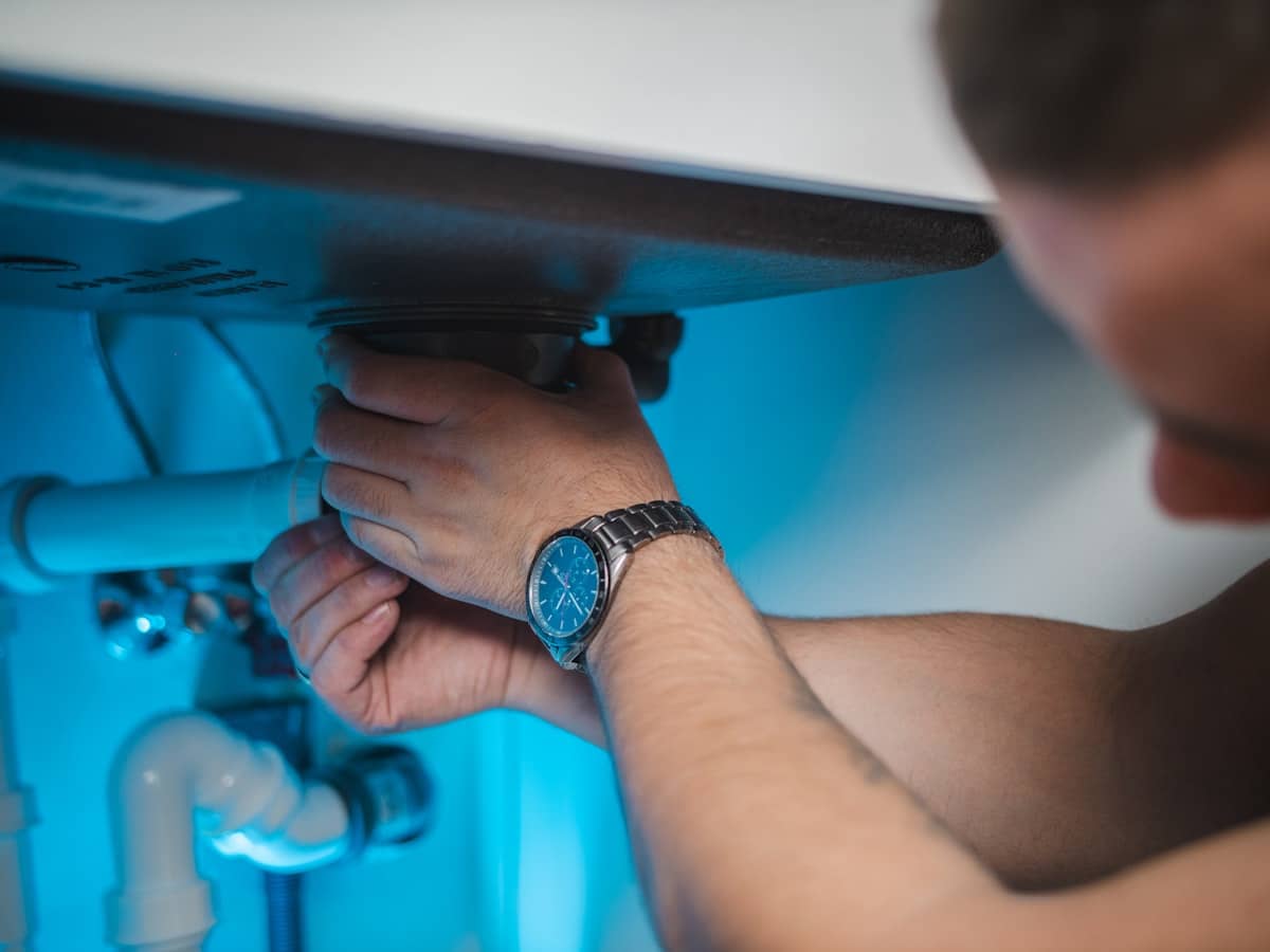 Plumber's hands tightening a drain fitting under a sink