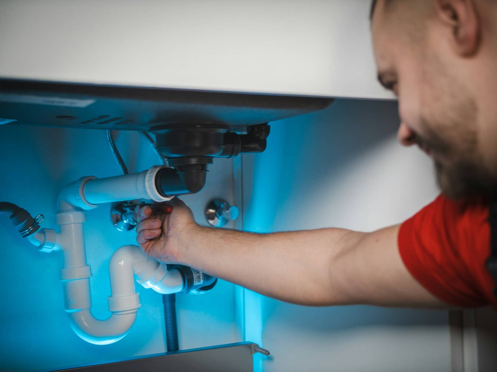 Plumber reaching into an under-sink cabinet to repair a leaking drain trap