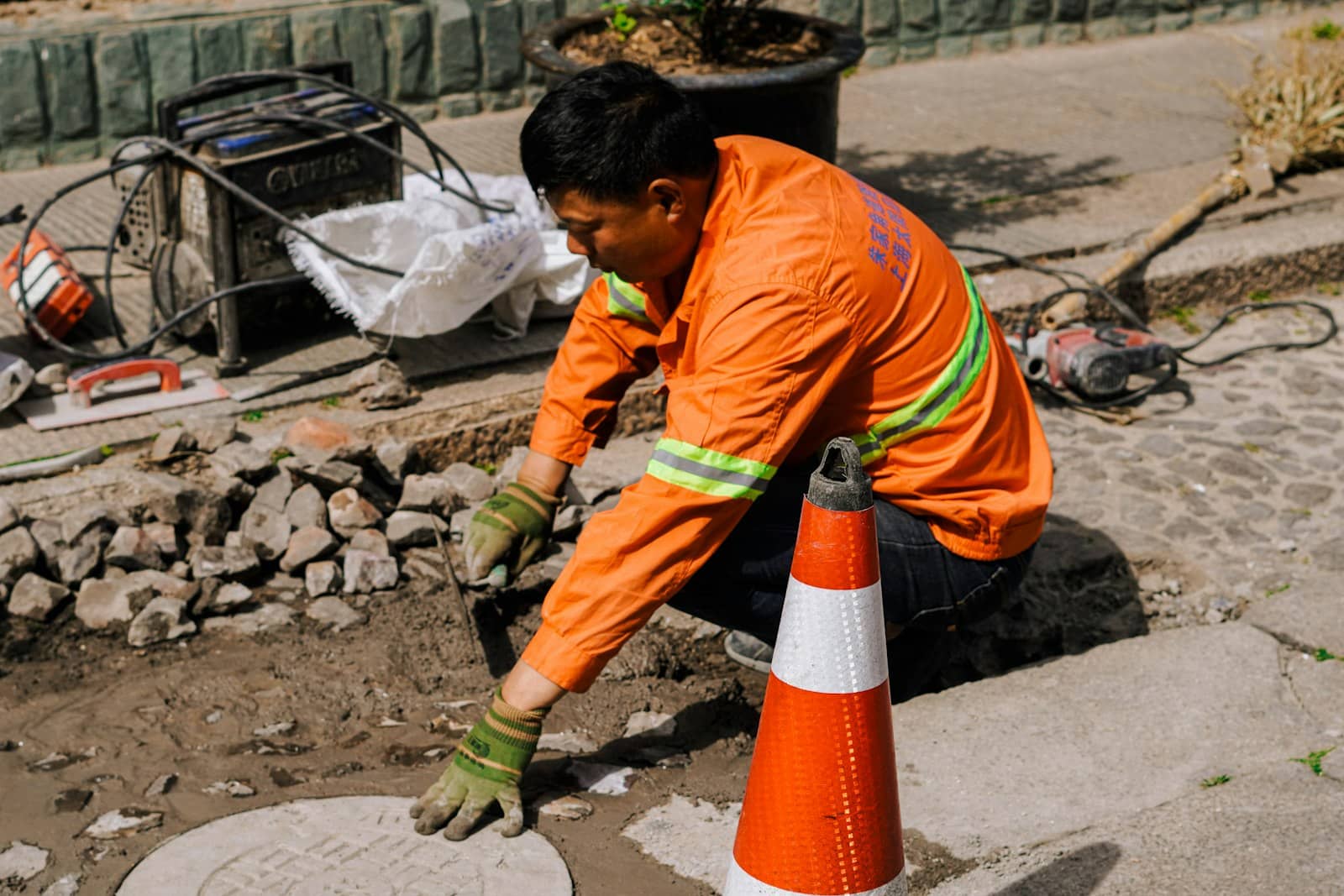Utility worker in orange work gear repairing a sewer access point at street level