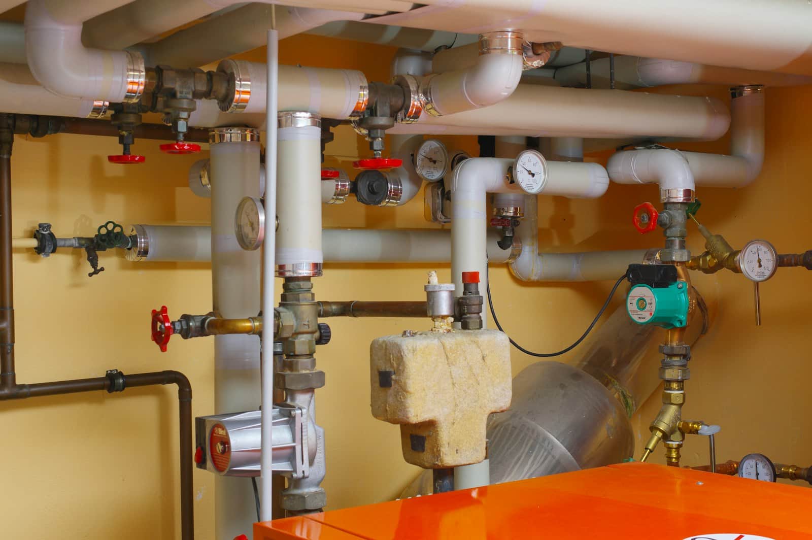 Basement mechanical room with pumps, valves, and insulated pipework